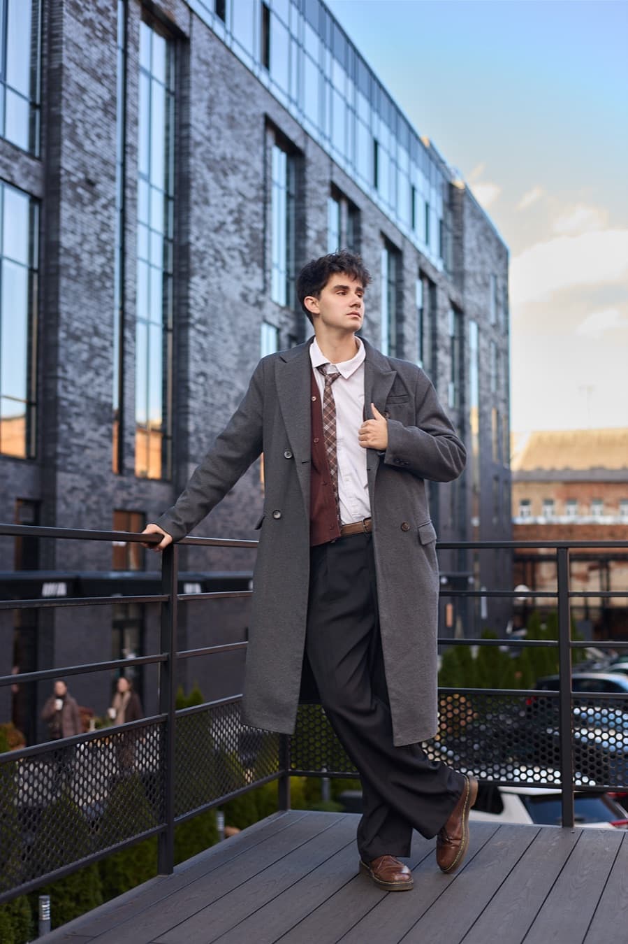 Rooftop frame at dusk, grey overcoat against a glass facade